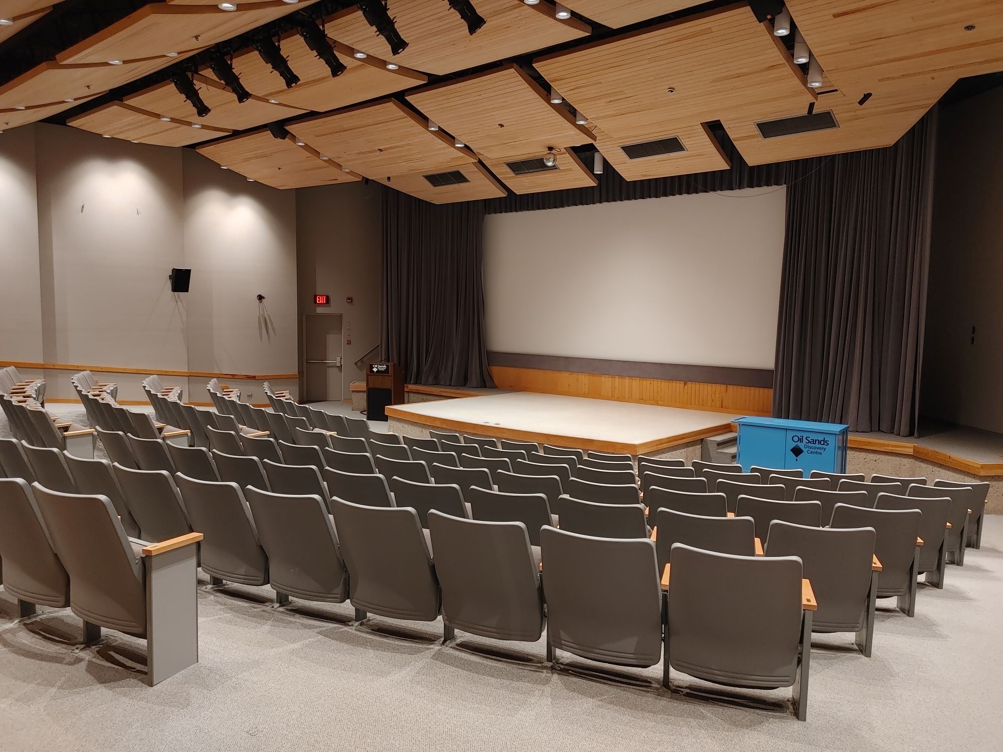 Theatre with fixed seating and stage plus screen at front of room.